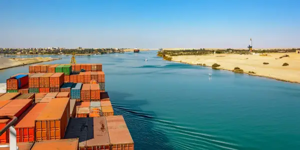 Containerrieschiff fährt durch den Suezkanal, ein Meisterwerk des Suezkanal Baus, vorbei an Wüstenlandschaft und Stadt.