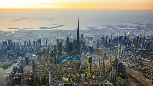 Luftaufnahme von Dubai bei Sonnenuntergang. Der Burj Khalifa ragt empor, umgeben von Wolkenkratzern und den künstlichen Inseln. Ein Blick auf die Dubai Besonderheiten.